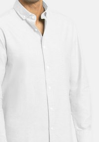 Camisa blanca de botones hecha de tela ligera, con un cuello clásico y mangas largas con puños abotonados. Textura suave, con un detalle mínimo.