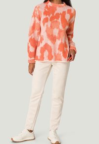 Mönstrad stickad tröja i orange och rosa med långa ärmar och rundad halsringning, parat med krämfärgade byxor och vita sneakers.