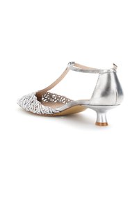Zapato de tacón kitten plateado con tira en T, frente tejido y parte trasera metálica cerrada sobre fondo blanco.