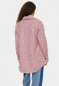 Roza in črna karirana srajčna jakna s frayed robovi in ohlapnim krojem. Narejena iz teksturirane tkanine, z značilnim ovratnikom in dolgimi rokavi.