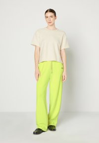 Top corto a maniche corte beige con texture abbinato a pantaloni da jogging larghi in un vivace verde neon con coulisse. Modella che indossa scarpe nere.