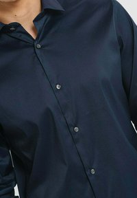 Camicia button-up blu navy realizzata in tessuto morbido, con colletto classico e sei bottoni, e una silhouette snella e aderente.