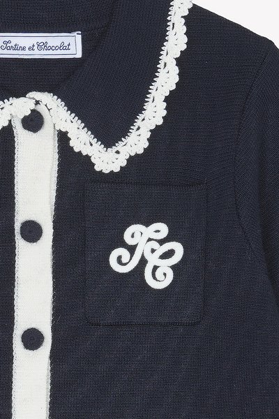 Námořnický svetr s bílým límečkem a knoflíky, se dvěma kapsami na hrudi a vyšitými iniciály "JC". Texturovaná látka s jemnými detaily.