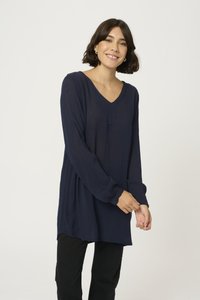 Blusa lunga a maniche con scollo a V, in tessuto texturizzato, con polsini abbottonati e vestibilità morbida. Abbinata a pantaloni neri.