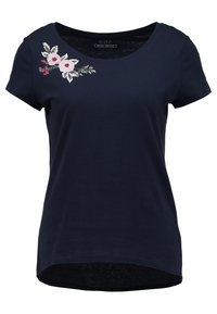 Camiseta de mujer de manga corta en color navy con cuello redondo y flores bordadas en rosa y blanco en el hombro izquierdo.