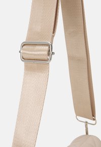 Beige stofrem med en glat, struktureret overflade og en sølvmetalknap, der har diagonale syninger. Ideel til tasker.