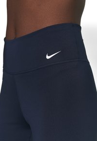 Granatowe legginsy o wysokim stanie wykonane z elastycznego materiału, z małym białym logo Nike na pasku. Gładka faktura z minimalną ilością szwów.