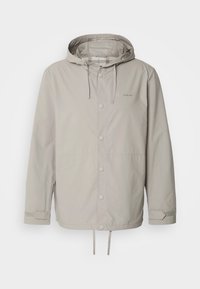 Jasno beżowa kurtka z kapturem, zapinana na zamek błyskawiczny z przodu, z regulowanymi mankietami, sznurkiem w kapturze i u dołu, oraz małym logiem na piersi.