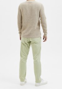 Beiger Strickpullover mit Struktur und langen Ärmeln, kombiniert mit hellgrünen, locker sitzenden Hosen und weißen Turnschuhen, von hinten betrachtet.