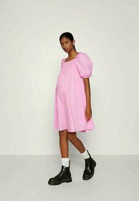 Vestido de maternidade rosa com mangas balão, decote quadrado, até ao joelho, feito de um tecido leve, combinado com botas de tornozelo pretas e meias brancas.