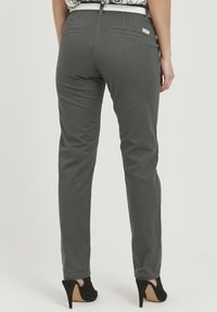 Pantalons de yoga gris avec une coupe ajustée, comportant des poches arrière, des détails de couture subtils et une texture lisse. Portés avec des talons hauts noirs.