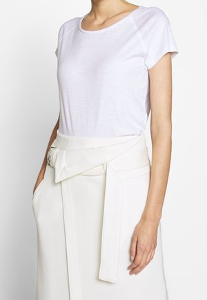 Biały T-shirt z krótkim rękawem o luźnym kroju, zestawiony z kremową spódnicą kopertową z szerokim paskiem i bocznymi kieszeniami. Gładka faktura.