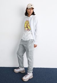 Casual outfit featuring a gray hoodie, striped button-up shirt, cargo sweatpants, and beige sneakers with red and gray accents.