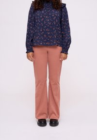 Blusa floreale navy con spalle arricciate, abbinata a pantaloni flared rosa polvere e scarpe nere. La blusa ha maniche lunghe con polsini arricciati.