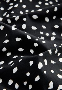 Fekete szövet sima textúrával, szabálytalan méretű fehér foltokkal díszítve, kontrasztos mintát alkotva.