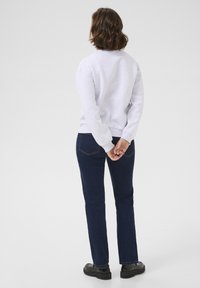 Grijze sweatshirt met ribbels aan de mouwen, blauwe denim jeans met een rechte pasvorm en discrete achterzakken, aangevuld met zwarte schoenen.