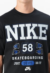 Juoda medvilninė marškinėliai su ryškiais baltais ir mėlynais grafikos elementais, įskaitant žodį "NIKE", numerį "58" ir "SKATEBOARDING."