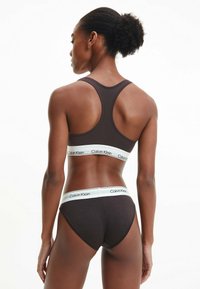 Bralette de algodón marrón y ropa interior tipo hipster a juego, con bandas elásticas blancas que llevan el logo de "Calvin Klein", diseño de espalda nadadora y textura suave.