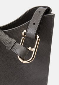 Sac à main en cuir gris avec une surface texturée, un accent en métal doré et une sangle avec des trous réglables pour la longueur.