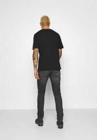 Zwart T-shirt met korte mouwen bekeken van achteren, met een klassieke pasvorm. Draag het met donkergrijze jeans en zwarte schoenen.