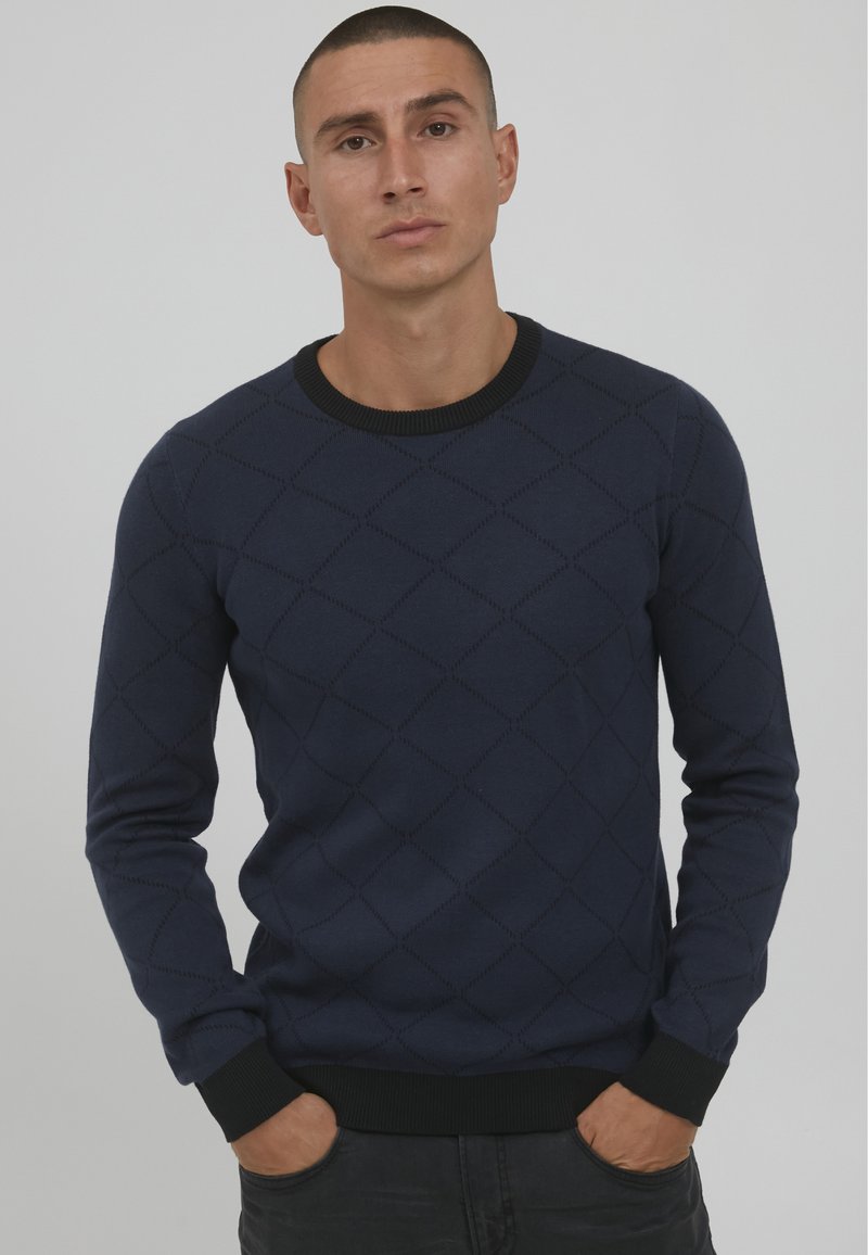 Navy knitted sweater with a diamond pattern, ribbed crew neckline, and cuffs. Features a smooth texture and fitted silhouette.