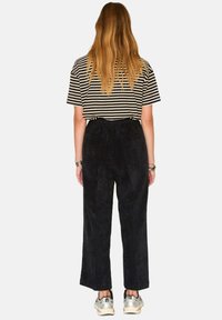 Chemise à manches courtes rayée, pantalon large en velours côtelé noir et chaussures de course argentées, vues de dos. Texture lisse et coupe décontractée.