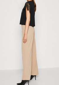 Top corto negro con acentos de manga de encaje, combinado con pantalones de pierna ancha beige y botas de tacón alto negras. Textura de tela suave.