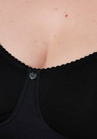 Černá podprsenka z hladkého materiálu, s vroubkovanými okraji, zapínáním na knoflík vpředu a hlubokým výstřihem.