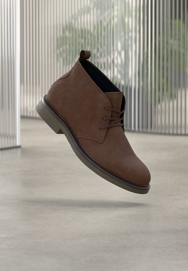 Rudos spalvos zomšiniai aulinukai su apvalia nosimi, užsegami raišteliais priekyje ir grublėtu pilkos spalvos padu. Gale yra mažas kilpelė, skirta lengvesniam užsimaudymui.