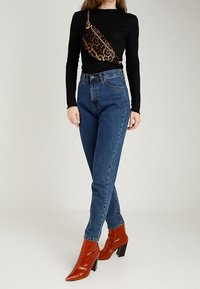 Jeans blu a vita alta, maglia nera a maniche lunghe e stivali rossi con tacco a punta; completati da una borsa a tracolla con stampa leopardata.