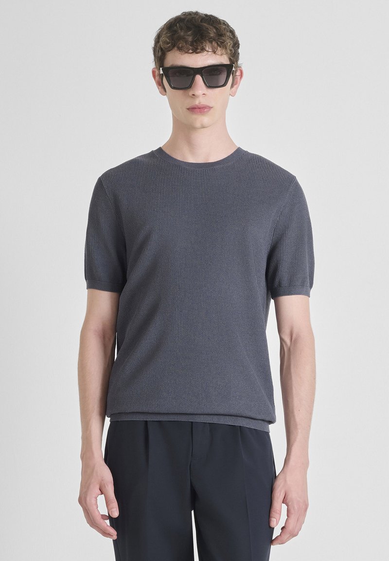 Majica s kratkim rukavima, okruglog izreza, tamnosiva, teksturirana pletenina, u kombinaciji s crnim sunčanim naočalama, nosi se uz široke tamne hlače.