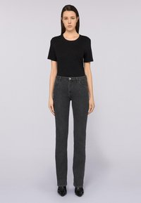 Camiseta negra de manga corta combinada con jeans grises oscuros de pierna recta y cintura alta. Conjunto completado con zapatos negros de puntera afilada.