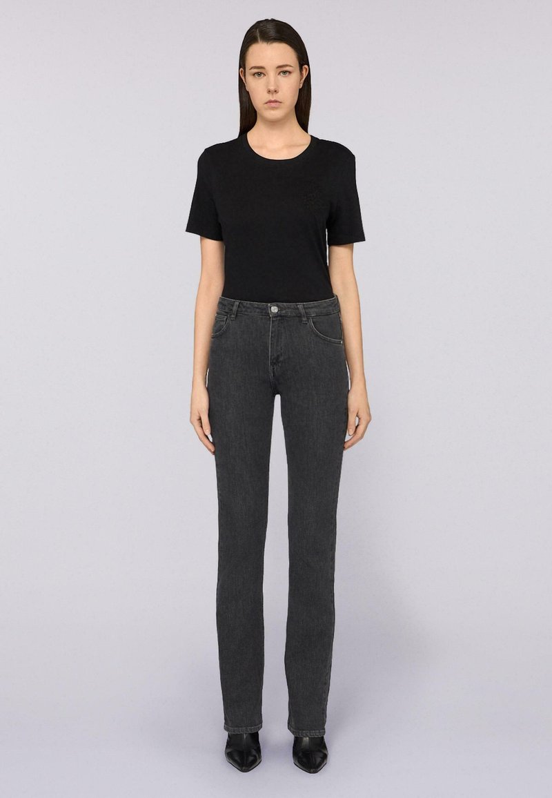 Camiseta negra de manga corta combinada con jeans grises oscuros de pierna recta y cintura alta. Conjunto completado con zapatos negros de puntera afilada.