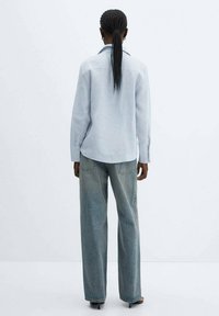 Chemise bleu clair à manches longues avec un col boutonné, associée à un jean bleu clair ample et décoloré. Le tissu semble doux avec une texture lisse.