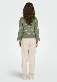 Žalias megztinis su baltomis širdelėmis, laisvas kirpimas ir plačios rankovės, derinamas su smėlio spalvos laisvomis kelnių.