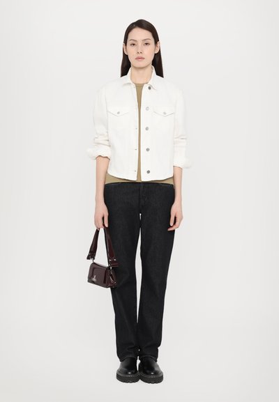 Chaqueta de mezclilla blanca sobre una blusa beige, combinada con pantalones anchos negros y zapatos de plataforma negros. Sosteniendo un pequeño bolso de charol burdeos.