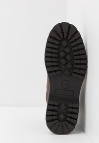 Suela de bota de cuero marrón, con un resistente dibujo de goma negra que presenta profundas ranuras y patrones en forma de diamante. La talla indicada es 42.