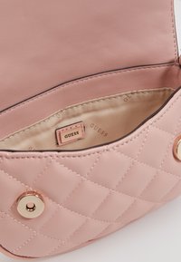 Różowa pikowana skórzana torebka z złotym zatrzaskiem, beżową podszewką z nadrukiem "GUESS" oraz małą firmową etykietą wewnątrz.