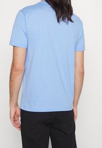 Jasnoniebieska koszulka z krótkim rękawem wykonana z bawełny, z okrągłym dekoltem i gładką fakturą, z prostym dołem w talii.