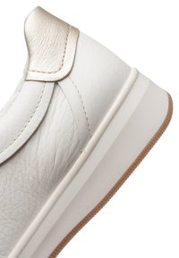 Witte leren sneaker met textuur, beige metallic hielstuk en dikke witte zool met bruine rubberen buitenzool.