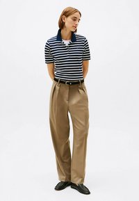 Marineblauw-wit gestreept poloshirt met een kraag, gecombineerd met beige wijde pantalon met hoge taille en zwarte leren loafers.