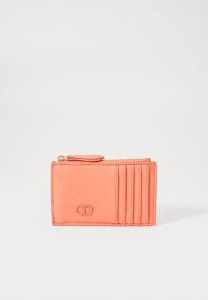 Portefeuille en cuir corail avec fermeture éclair, comportant plusieurs emplacements pour cartes d'un côté et un détail logo embossé sur le devant. Texture lisse.