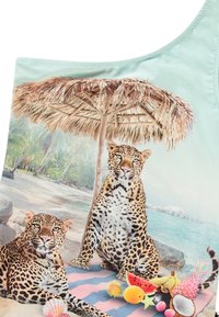 Top de fato de banho com um padrão tropical que apresenta duas leopardas, um guarda-sol de palha e diversas frutas sobre uma superfície em padrões azul e rosa.