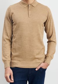 Beige poloshirt met lange mouwen en een kraaghalslijn, drie knoopsluitingen en een geribbelde onderrand, gemaakt van een zachte gebreide stof.