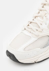 Κοντινό πλάνο ενός λευκού αθλητικού παπουτσιού με πλέγμα στα πλαϊνά, δερμάτινες επιστρώσεις, λευκά κορδόνια και μαύρη λαστιχένια σόλα στο μπροστινό μέρος.