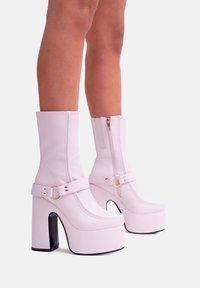 Stivali platform rosa con finitura lucida, punta tonda, altezza alla caviglia, zip laterale e una larga fascia con una fibbia circolare in evidenza.