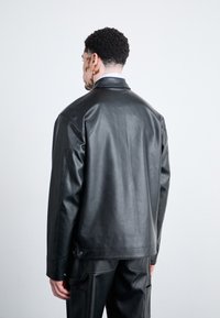 Veste en cuir noir avec une coupe décontractée, col pointu et texture lisse. Présente des coutures détaillées et des accents en métal.