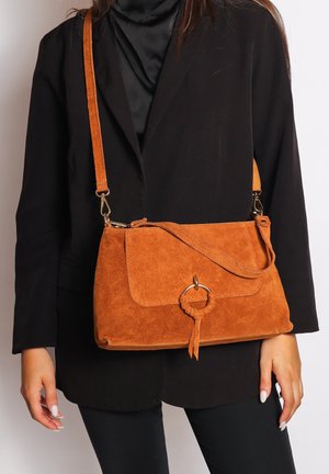 Borsa a tracolla in suede marrone con chiusura a patta, accentata da un anello circolare e una tracolla regolabile. Dimensione media con una texture morbida.