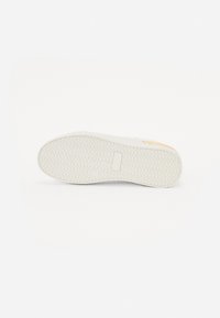 Biała podeszwa tenisówki z wzorem w zygzak, posiadająca gładką, fakturowaną powierzchnię oraz mały prostokątny akcent po boku.