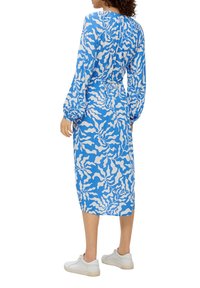 Sininen ja valkoinen kuvioitu mekko, jossa on pitkät hihat ja midi-pituus, vyötärö on istuva ja selässä on kerätty yksityiskohta, yhdistetty valkoisiin lenkkikenkiin.